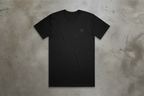 Black t-shirt with a small logo on a concrete floor