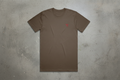 Brown t-shirt with a small red logo on a concrete background