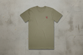 Olive green t-shirt with a small red logo on a concrete background