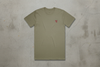 Olive green t-shirt with a small red logo on a concrete background